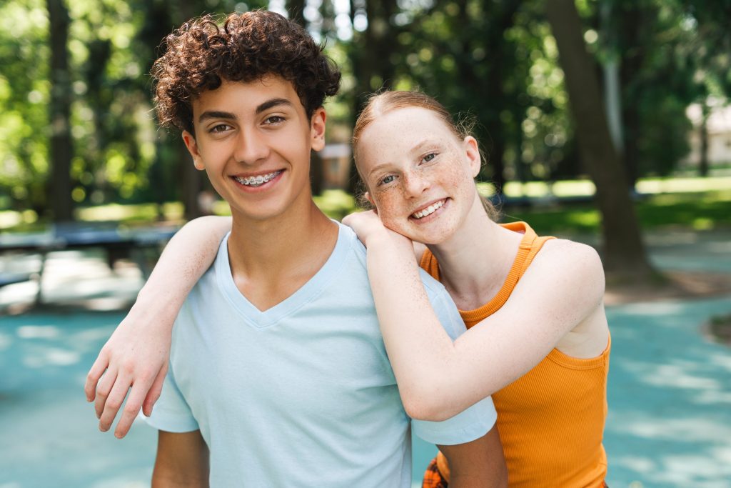 Portrait of happy red hair teenager girl hugging her male friend at the park.