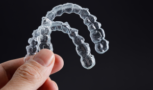 A hand holding a set of clear aligners in front of a black background