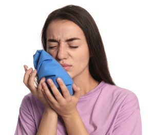 Young woman suffering from mouth pain, holding a cold compress on her cheek to relieve pain on white background