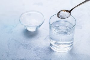 Spoon full of salt being poured into glass of warm water