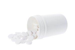 A sideways, white pill bottle spilling out pills onto white background