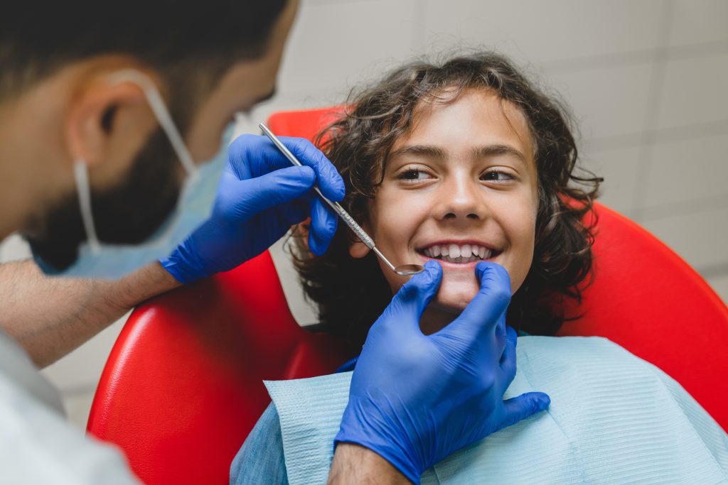 Close up shot of kid`s boy`s jaws, white healthy teeth while doctor stomatologist dentist making doing orthodontic checkup