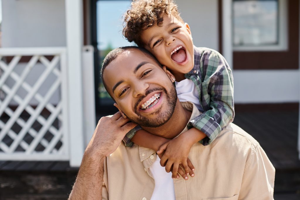Positive African American boy hugging excited father with braces