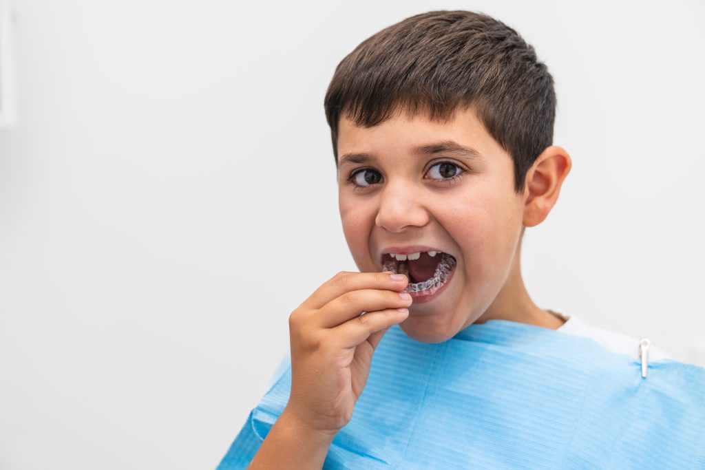 A boy inserts his clear aligner during an orthodontic appointment at the dentist. Concept of dental care for children and orthodontic treatments.