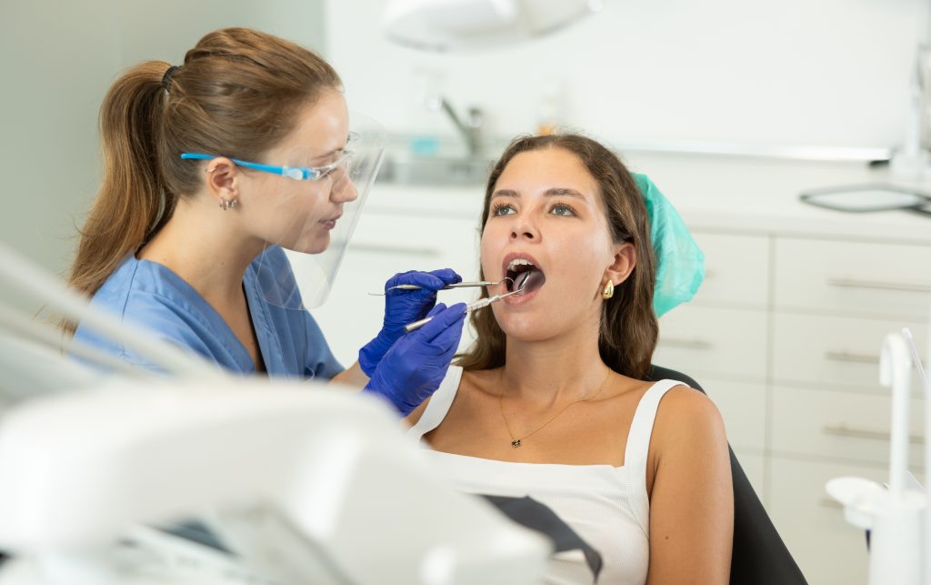 Young woman came for a consultation with an orthodontist to correct her bite and put braces. Female dentist carefully examining client teeth in dental clinic