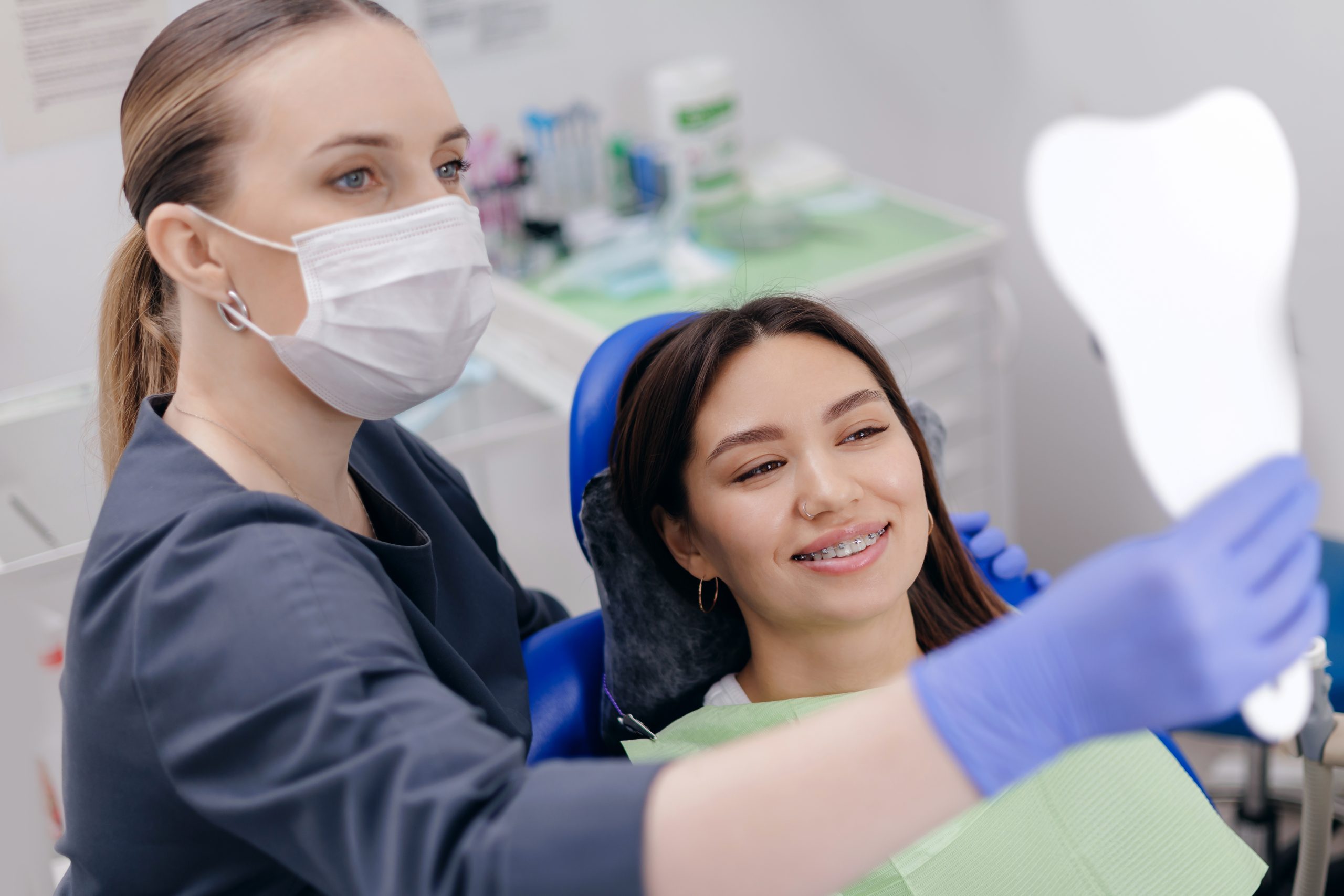 Female dentist assists asian young woman with dental checkup using mirror.