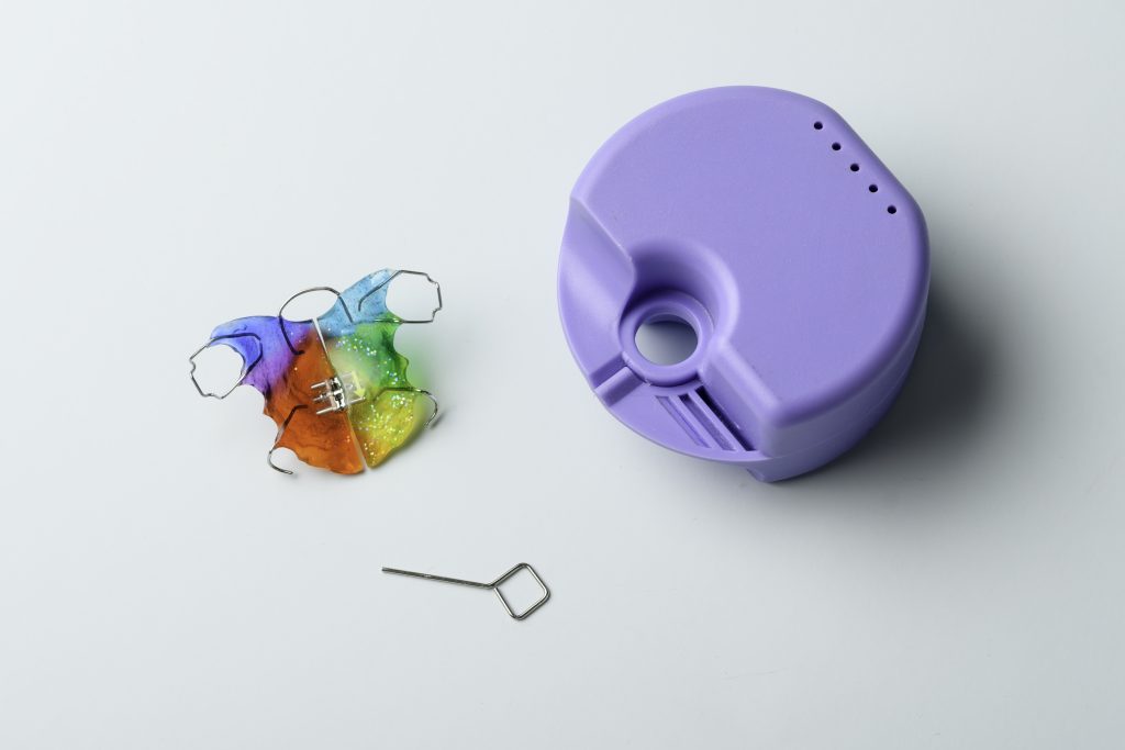 Colorful orthodontic expander retainer with purple storage case and metal expansion key on light blue background for dental aftercare.
