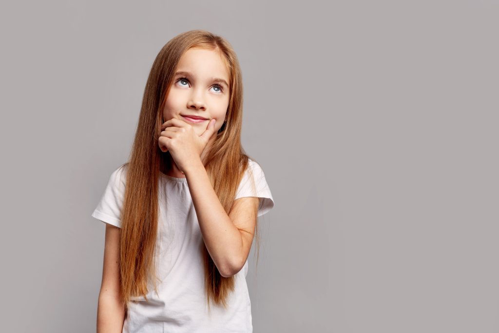 Beautiful thoughtful young girl with long hair looking up, isolated on gray studio background, expressing curiosity, imagination and creative childhood thinking in beauty child portrait