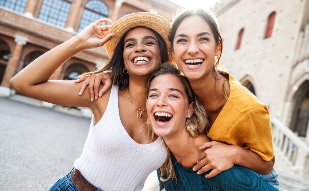 Three multiethnic girls having fun walking in city street - Happy young women laughing together enjoying summertime vacation